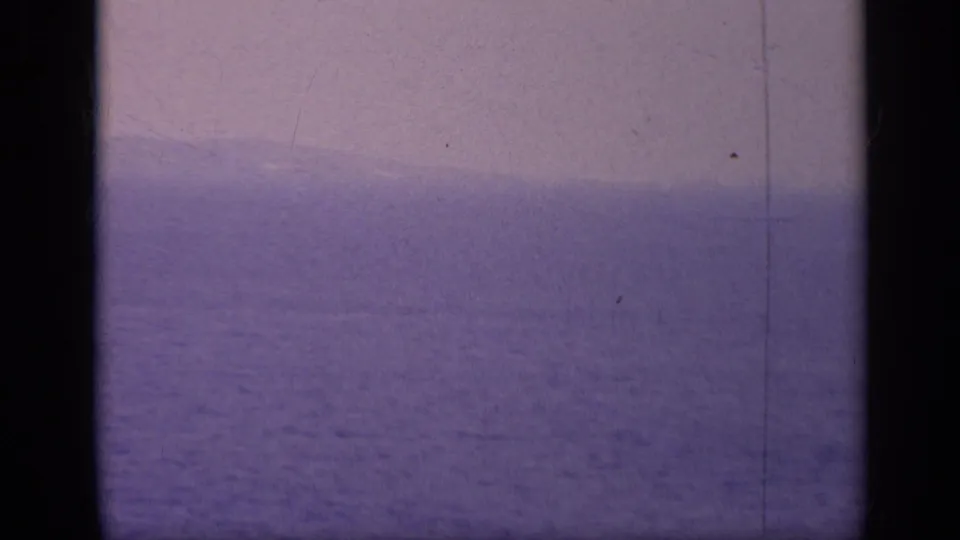 1962 Italy 8mm frame showing a distant warship-like silhouette on a hazy blue horizon with film-gate borders.