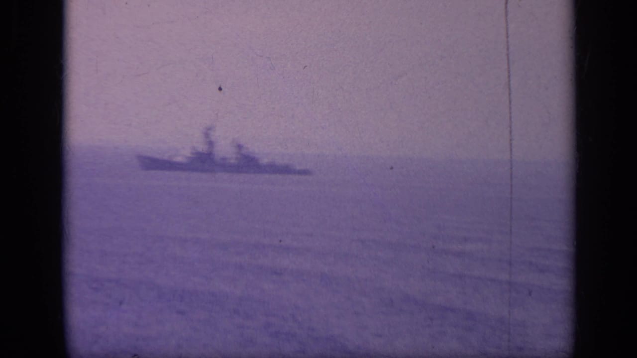 Warship silhouette on the horizon, framed by dark film borders.