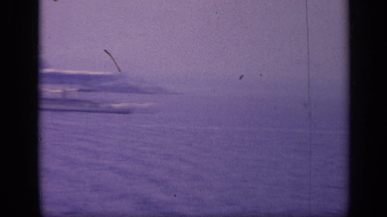 Purple-tinted open sea with a hazy horizon and faint distant shapes.