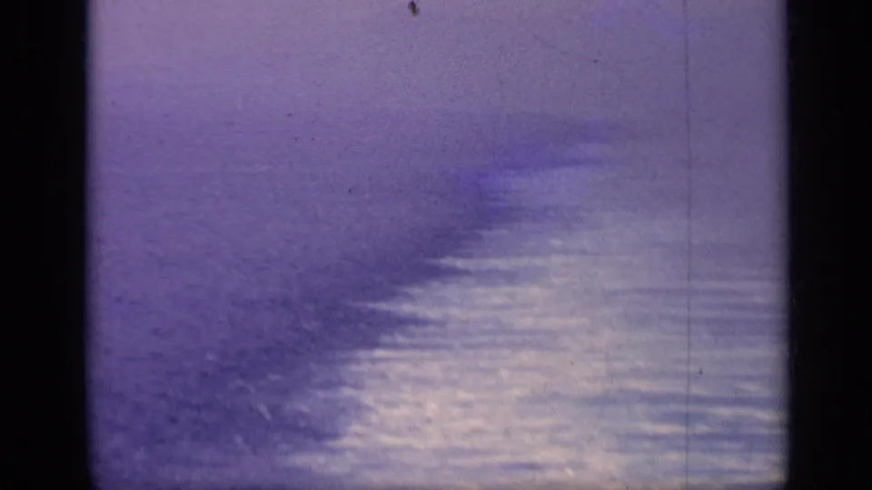 1962 Italy 8mm frame with reflective sea surface, haze, and soft distant forms that may be vessels near the horizon.