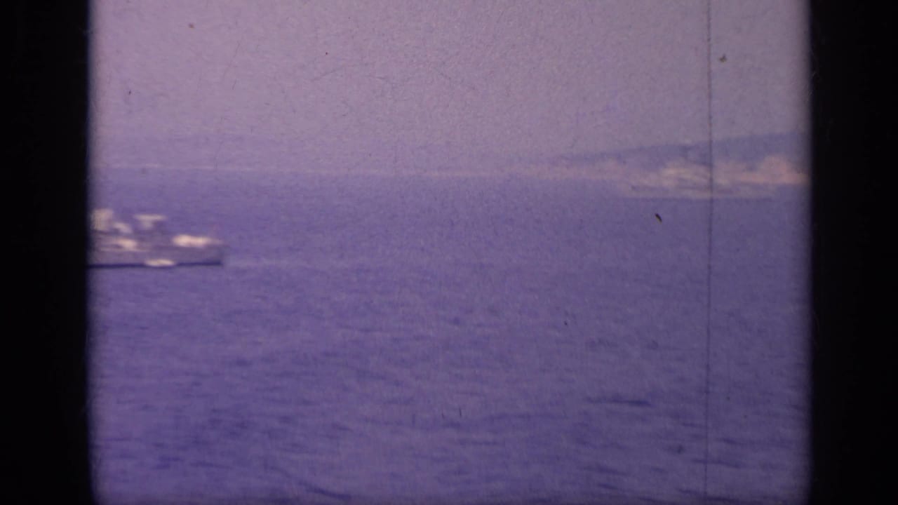 Distant ship on calm water with low coastline on the horizon.