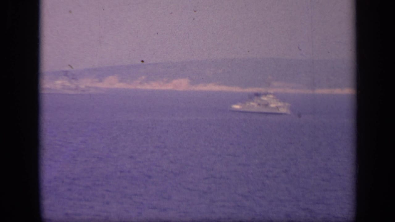 Naval-looking ship near a distant coastline across open water.
