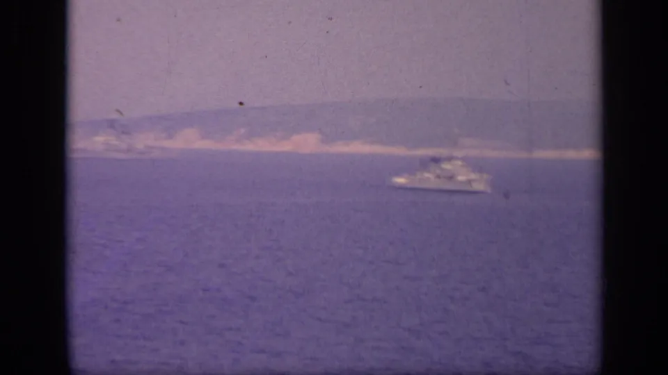 A naval-looking vessel appears near the horizon in 1962 Italian coastal footage, framed through dark film gate edges.