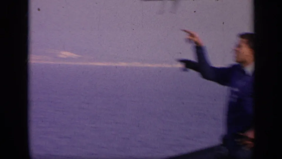 A person in dark clothing stands at the edge of a 1962 Italy coastal frame, pointing toward the distant water.