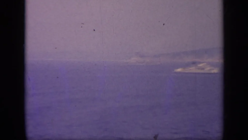 Soft 8mm frame of open water with a faint distant ship-like shape near the horizon, seen through haze.
