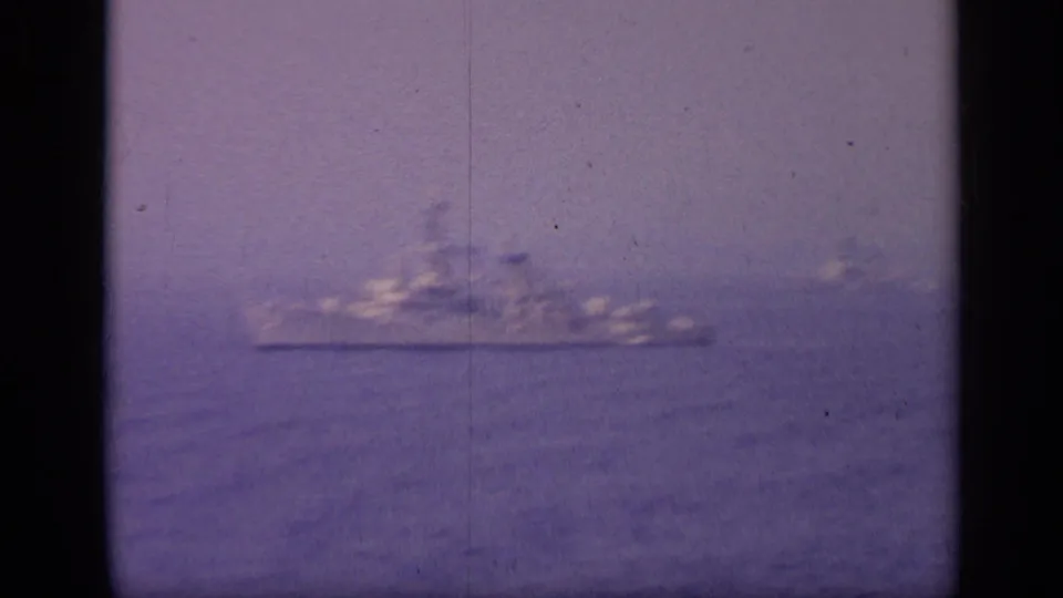 A large ship-like silhouette sits on the hazy sea horizon in grainy 1962 8mm footage from Italy.