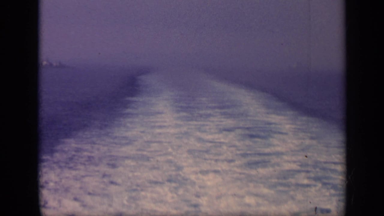 Foamy ship wake trailing across open water under a hazy sky.