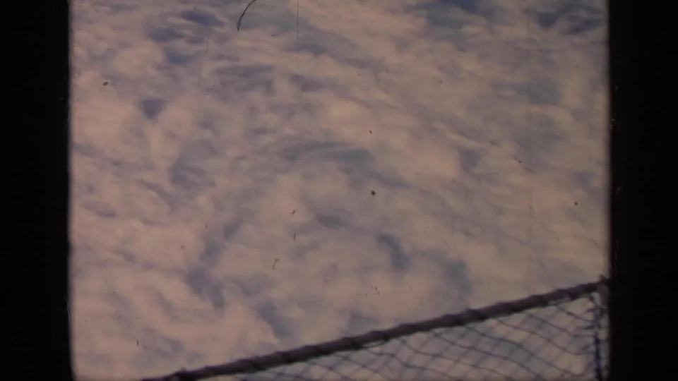1962 Italy 8mm frame showing foamy water beyond a diagonal chain-link railing from a moving vessel.