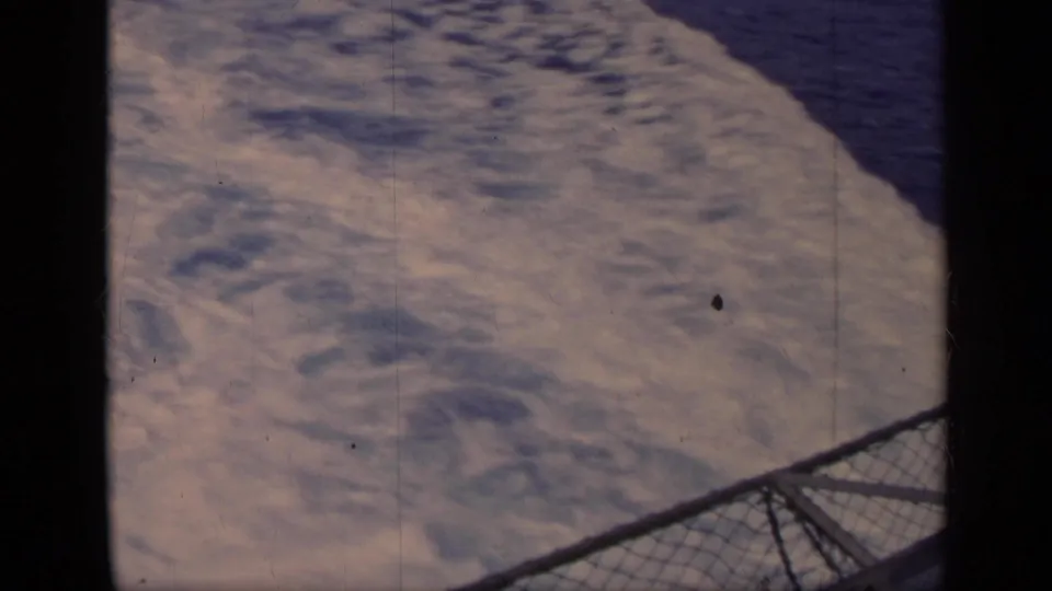 1962 Italy 8mm frame of rippled water seen past a chain-link boat railing and dark frame edge.