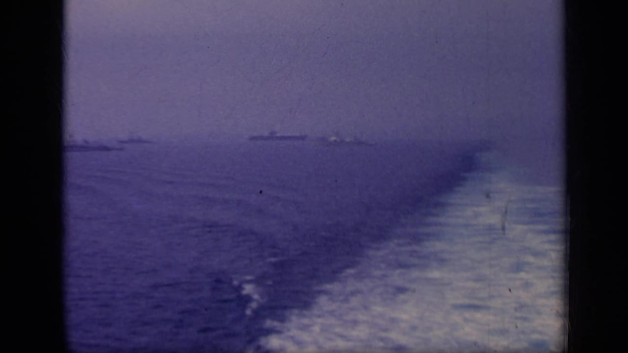 Distant ships on a hazy sea seen past the wake of a moving vessel.