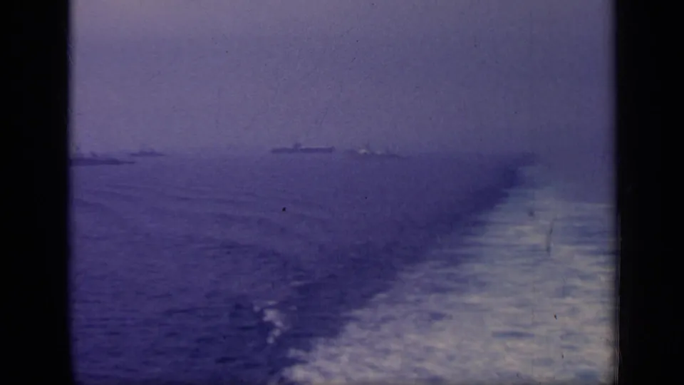 1962 Italy 8mm frame showing open water, a foamy ship wake, and distant naval vessels under a hazy sky.