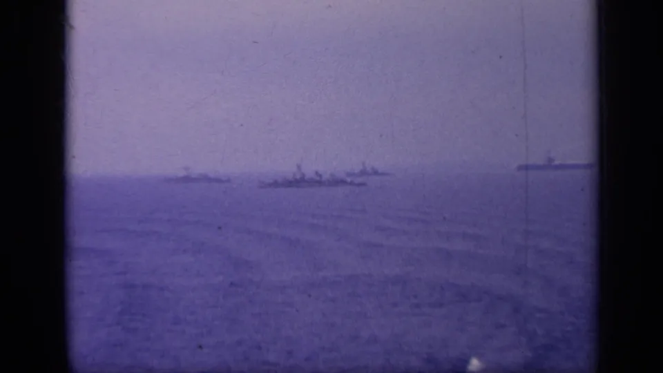 1962 Italy 8mm frame with distant naval ship silhouettes spread across calm sea beneath a hazy sky.