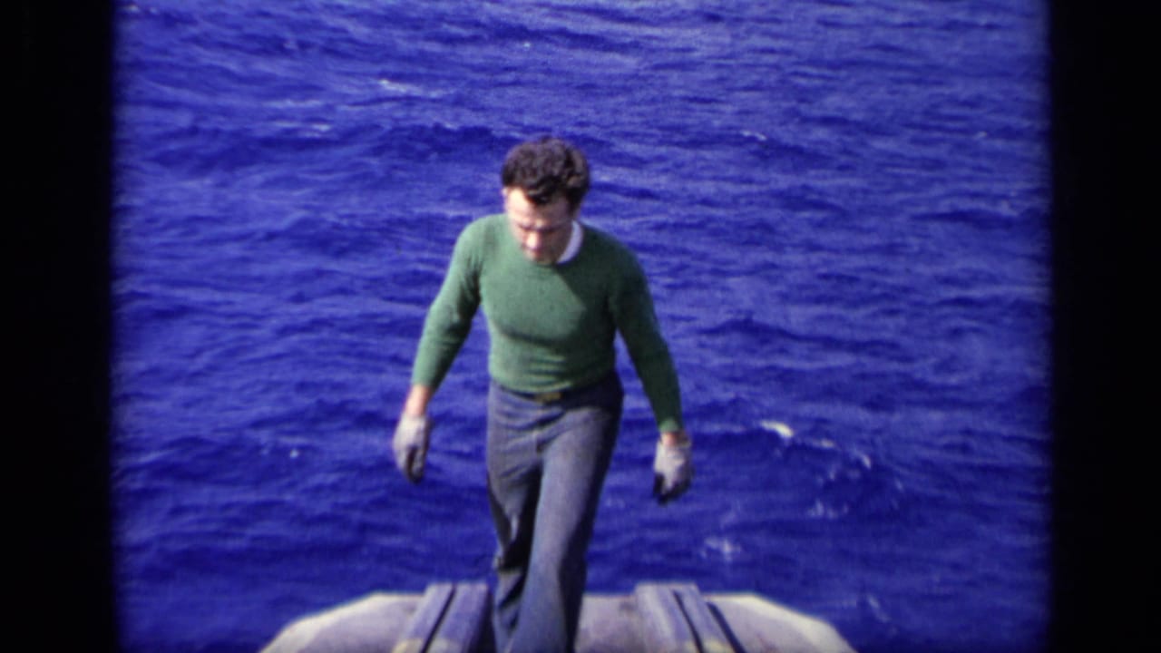 A man in a green sweater walks toward the camera along a vessel deck, with open ocean behind him in 1962 8mm footage.