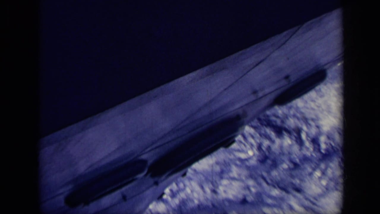 Blue-tinted view of a ship hull cutting through bright water behind dark vertical framing.