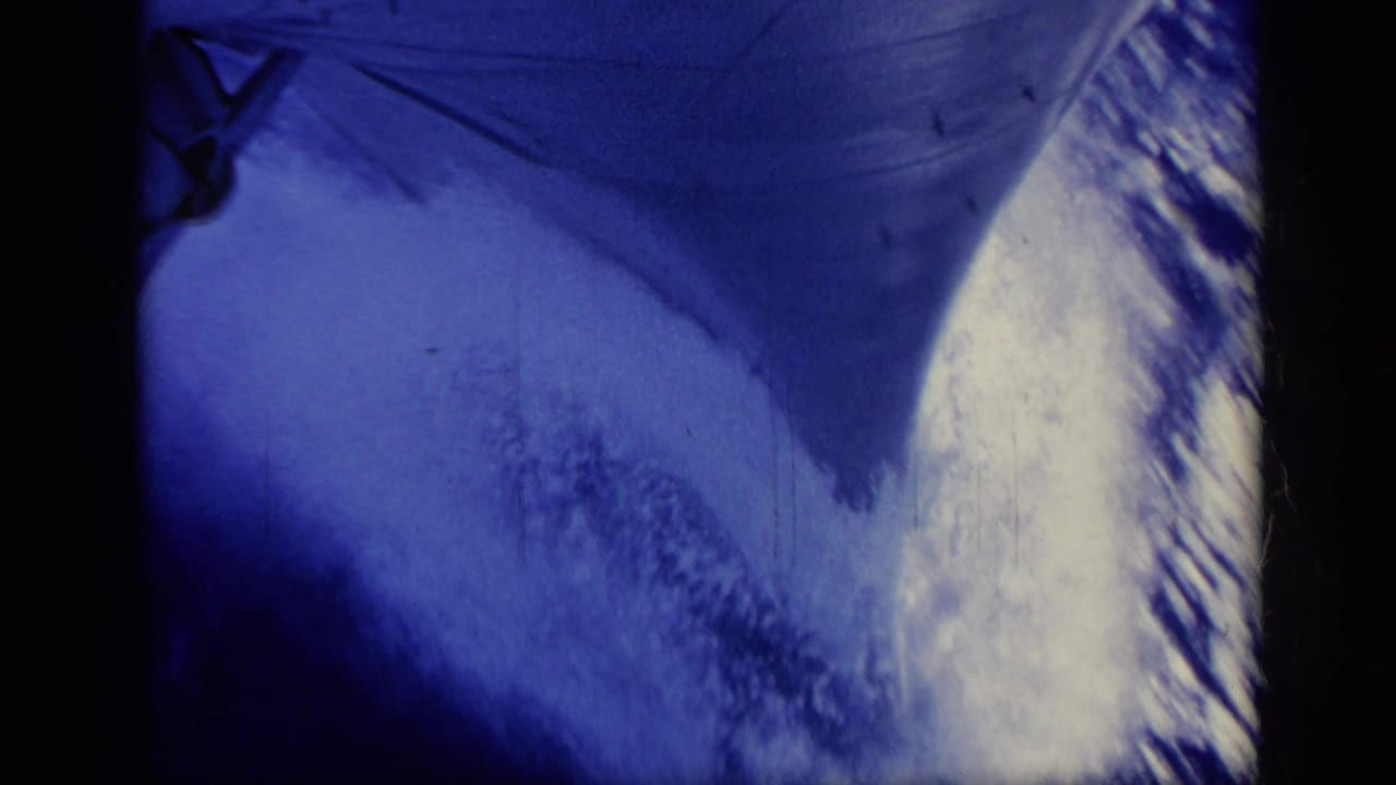 Blue-tinted 1962 Italy home-movie frame of a ship's bow cutting forward through bright, foamy water.