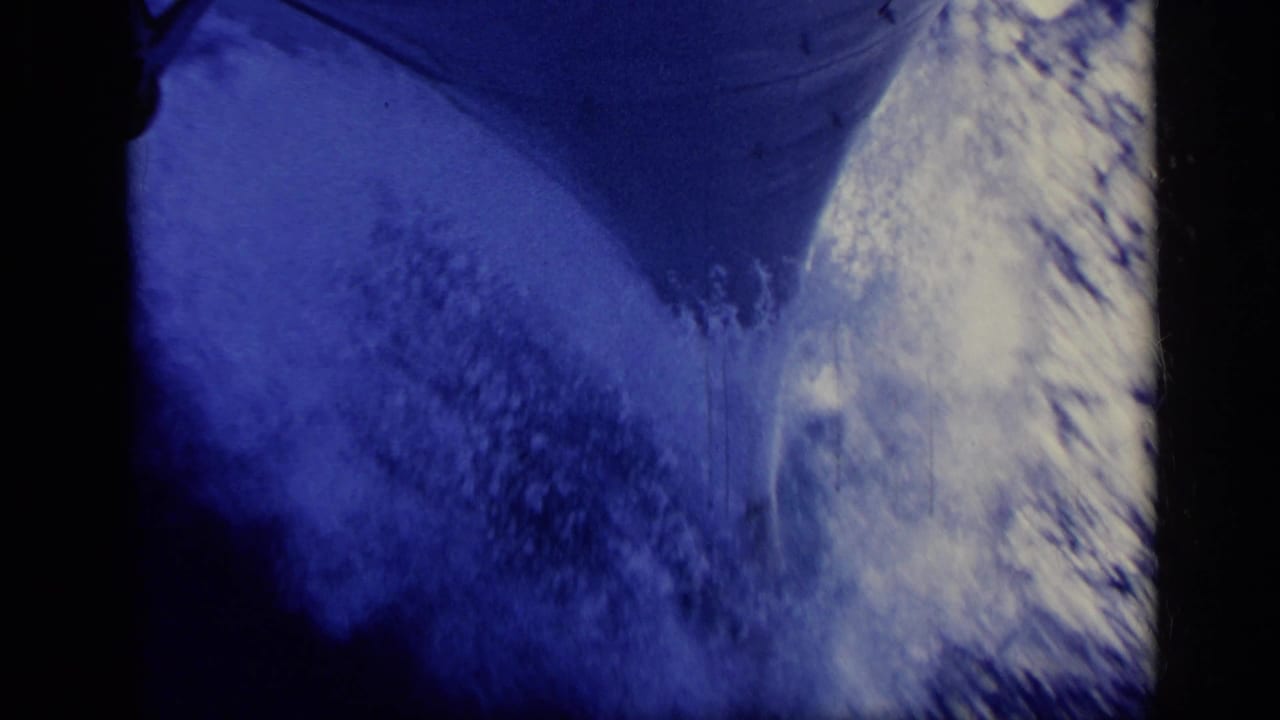 Blue-tinted close view of a ship hull beside foaming sea water.