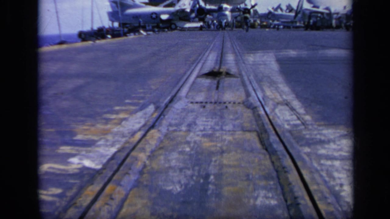 1962 Italy 8mm frame showing a carrier-style deck with aircraft lined up and deck tracks leading forward.