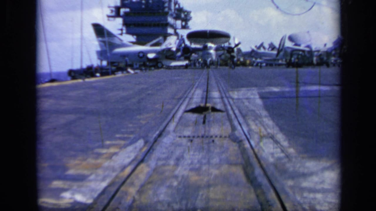 Carrier deck view with catapult rails leading toward parked propeller aircraft and the ship island.