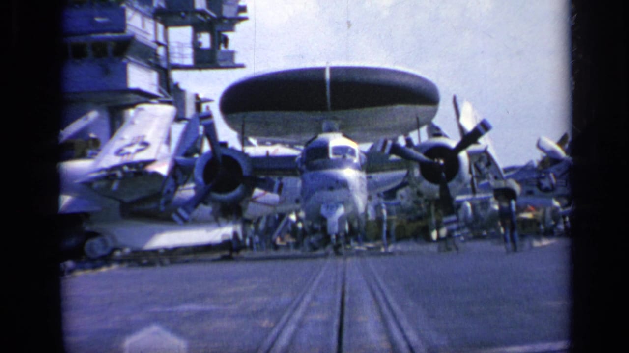 1962 Italy 8mm frame of a radar-equipped propeller aircraft on the carrier deck, with crew figures and nearby aircraft visible.