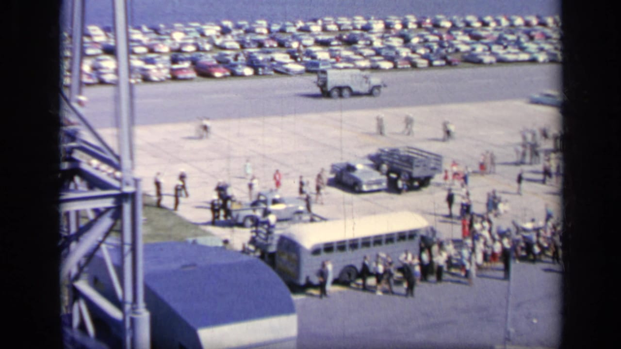 1962 Italy elevated tarmac view with buses, trucks, crowds, and rows of parked cars near an aviation area.