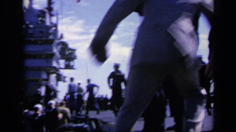 1962 Italy 8mm frame showing sailors in white uniforms moving across a warship deck near ship structures and distant personnel.