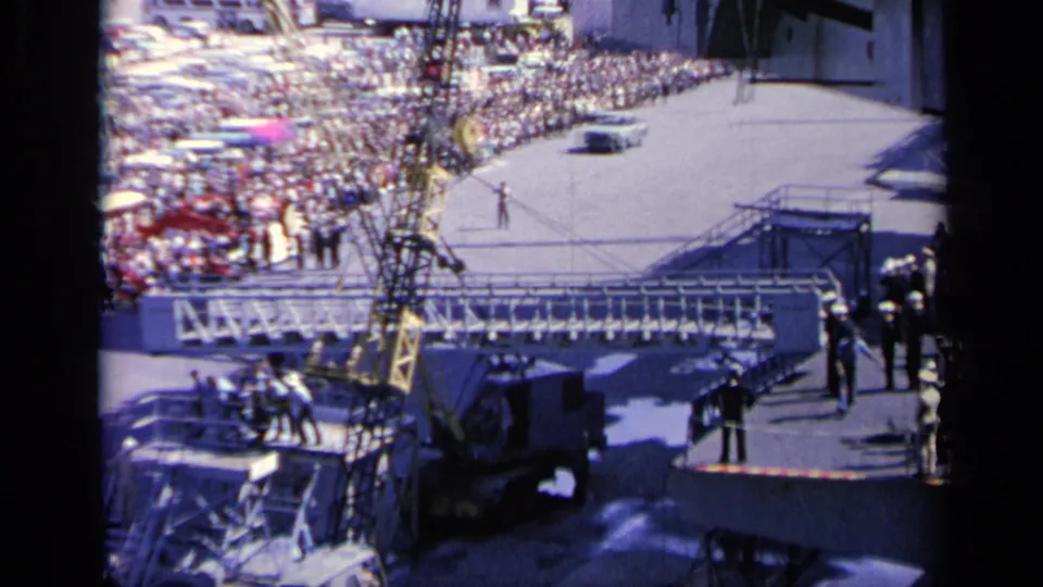 1962 Italy 8mm frame showing a crowded pier, crane structure, and shipboard equipment from a high deck viewpoint.