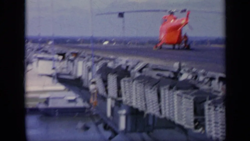A soft 8mm frame from Italy in 1962 showing a red helicopter on the deck area of a large ship during visible response activity.