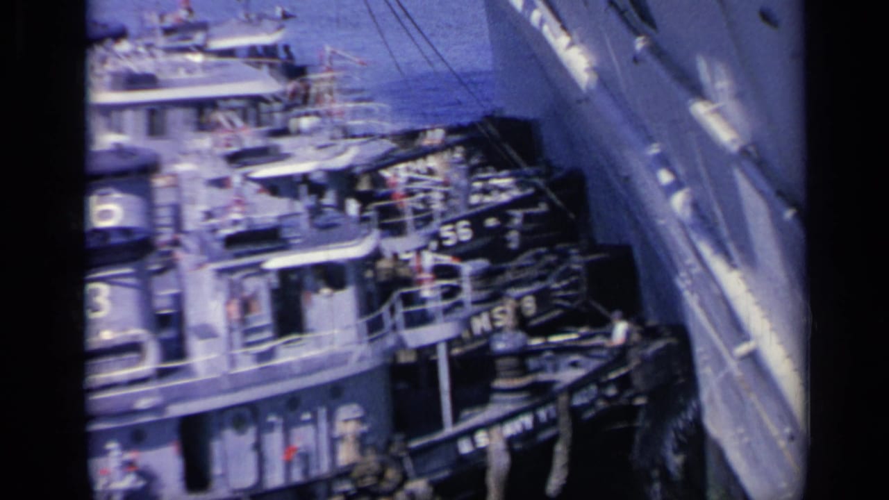 Numbered gray U.S. Navy tugboats crowded beside a larger vessel in blue harbor water.