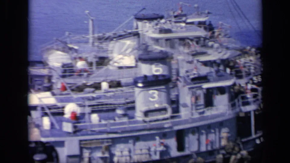 1962 Italy 8mm frame of Navy tugboats with numbers, railings, and crew figures clustered near a larger vessel.
