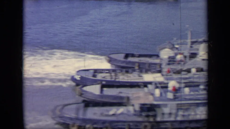 1962 Italy 8mm frame of a Navy tugboat partially cropped as white wake spreads across the harbor surface.