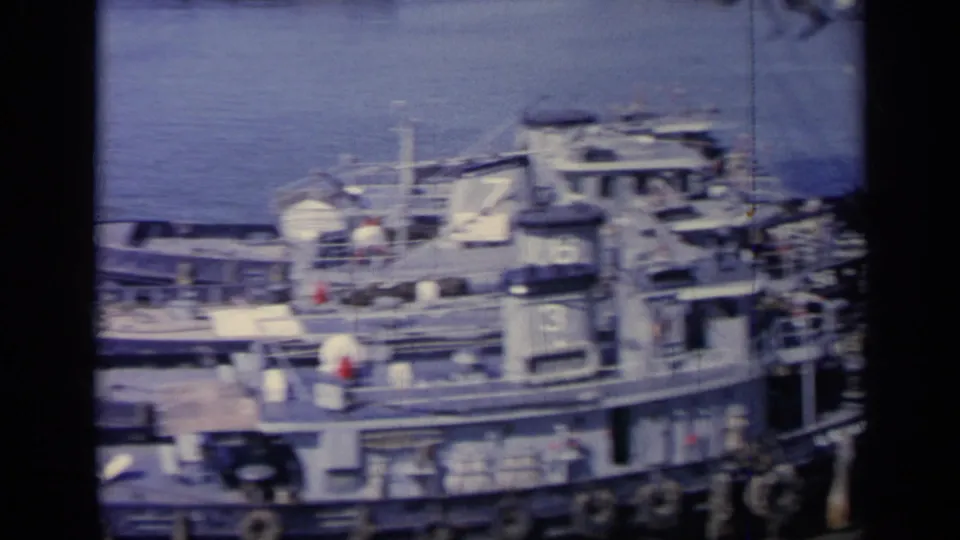 1962 Italy 8mm view of docked naval vessels with small numbered tugboats alongside a larger ship in harbor.