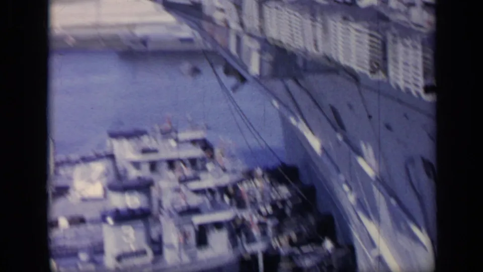 Elevated 8mm view across an Italian harbor with docked vessels, waterfront buildings, and a road or quay beside the water.