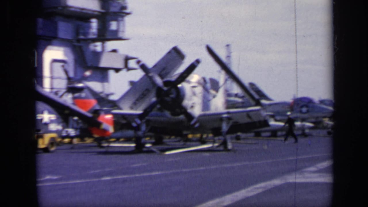 Carrier deck with parked propeller aircraft, crew figures, and the ship island in the background.