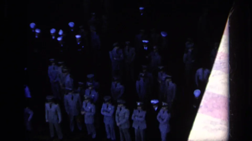 1962 Italy 8mm frame showing U.S. Navy personnel in formal uniforms under dark blue ceremony lighting.