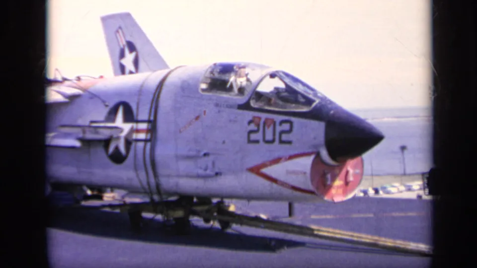 A U.S. Navy jet marked 202 sits on a carrier deck, with national insignia visible on the fuselage and tail.