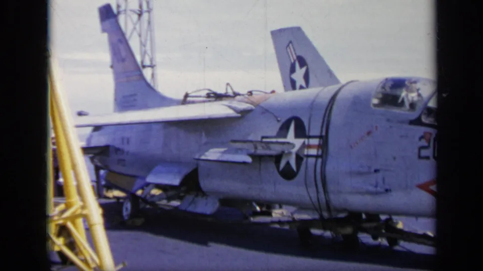 1962 Italy-labeled frame showing the side of a U.S. Navy jet with insignia, tail section, and carrier deck structures visible.