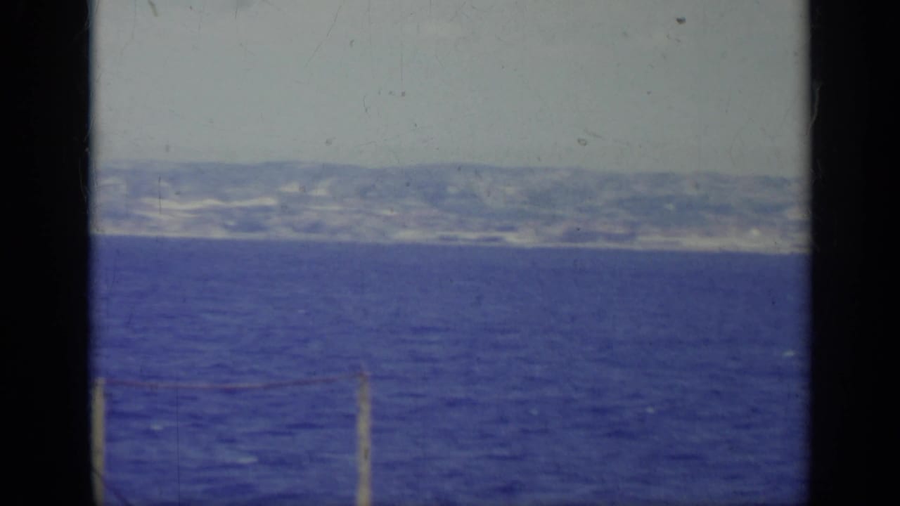 Blue water with a hazy shoreline and mountains beyond, framed by dark film edges.