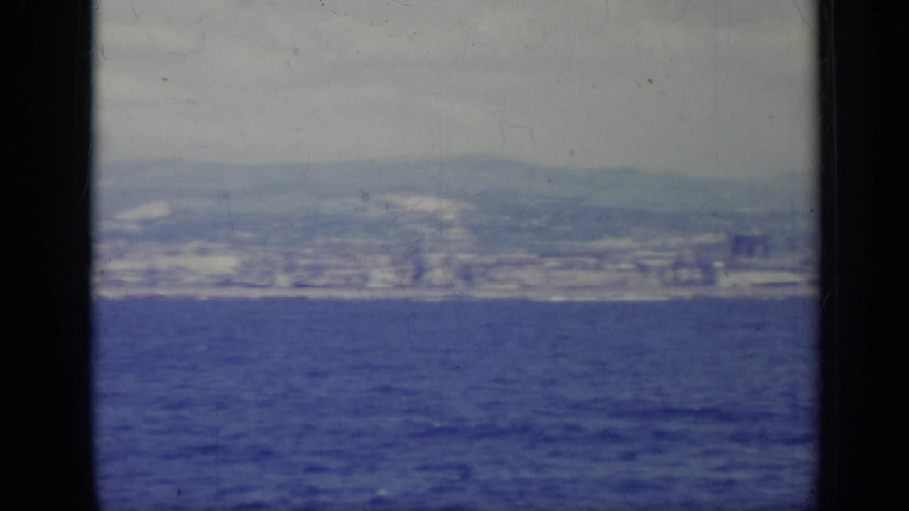Distant coastal city across blue water under a hazy sky.
