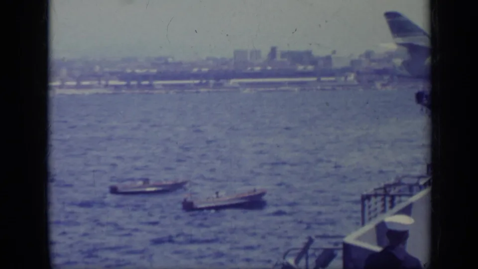 Two motorboats pass below a shipboard viewpoint, with hazy Italian shoreline and part of the vessel visible.