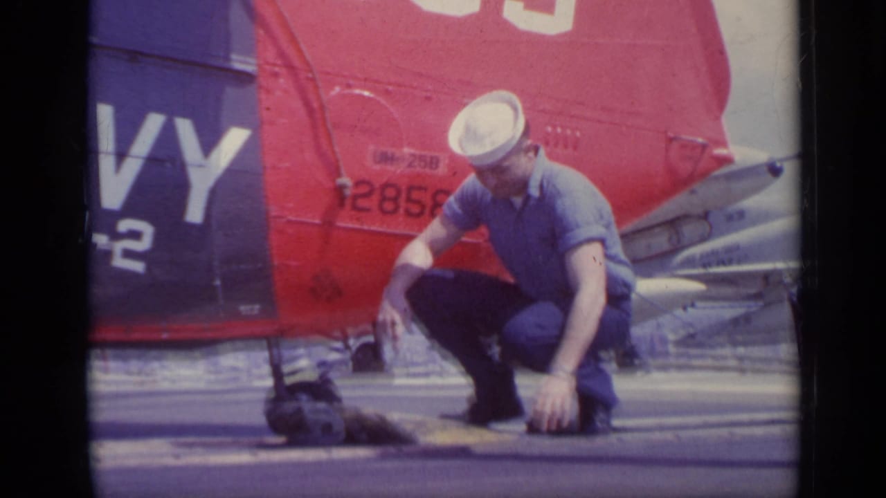 Sailor crouches beside a small animal near a red and blue Navy helicopter tail.