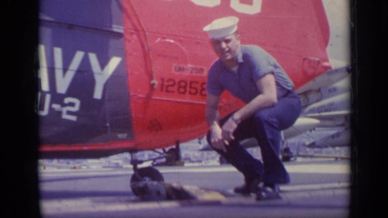 Sailor crouches and looks toward the camera near the helicopter tail.
