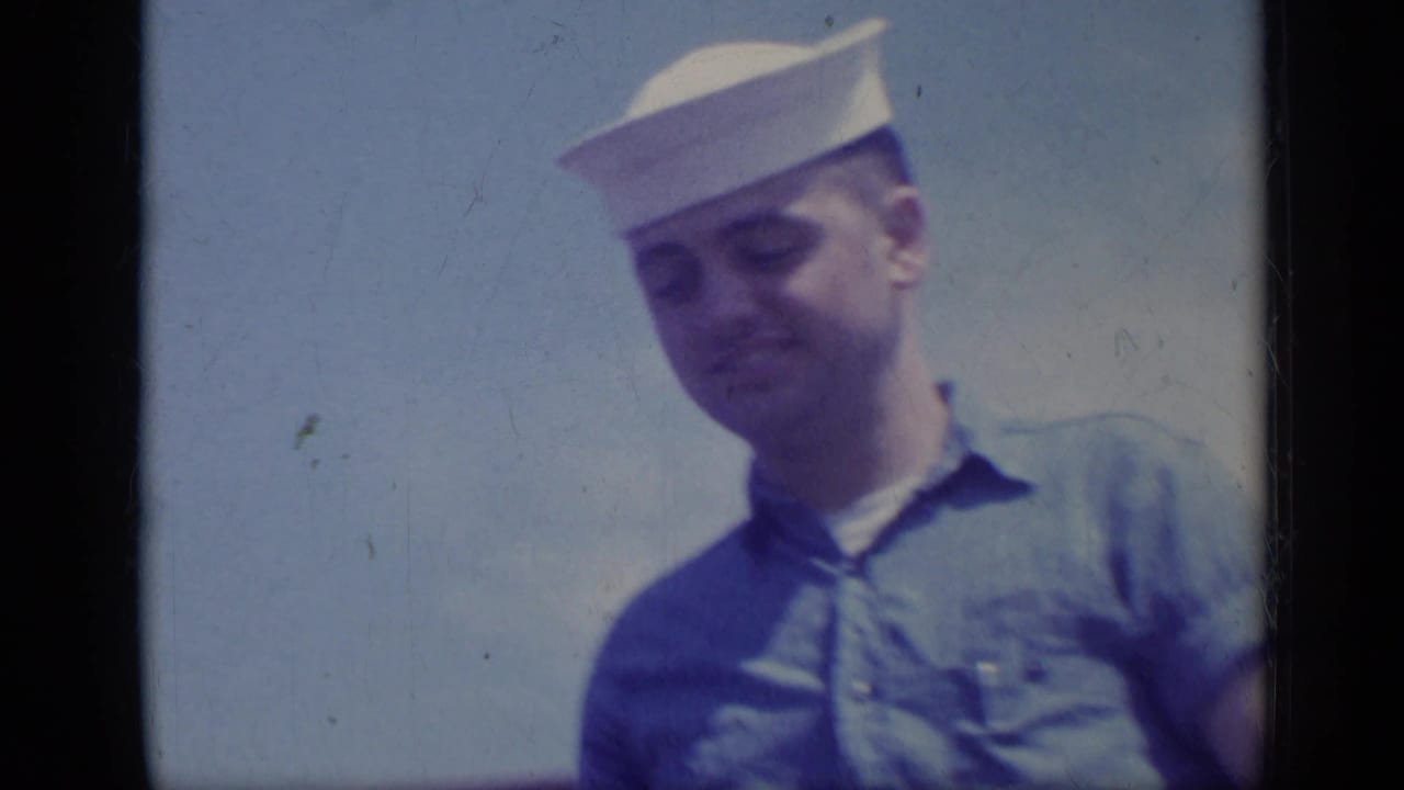 Close view of a sailor in uniform against a blue sky, framed by dark film borders.