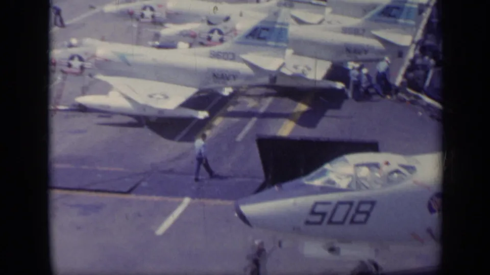 1962 Italy metadata-supported 8mm frame showing carrier-deck Navy jets, visible aircraft numbers, sailors near the rail, and a close jet nose marked 508.