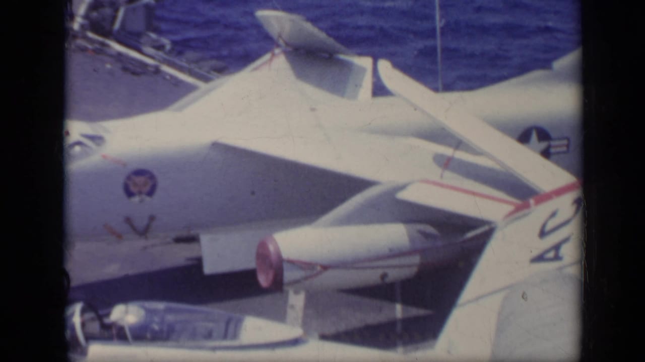 White U.S. Navy jet fighters parked tightly on an aircraft carrier deck with ocean beyond.