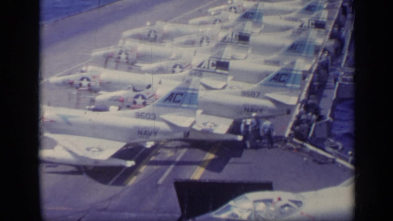 1962 Italy 8mm frame showing rows of parked Navy jets on an aircraft carrier deck with crew visible near the rail.