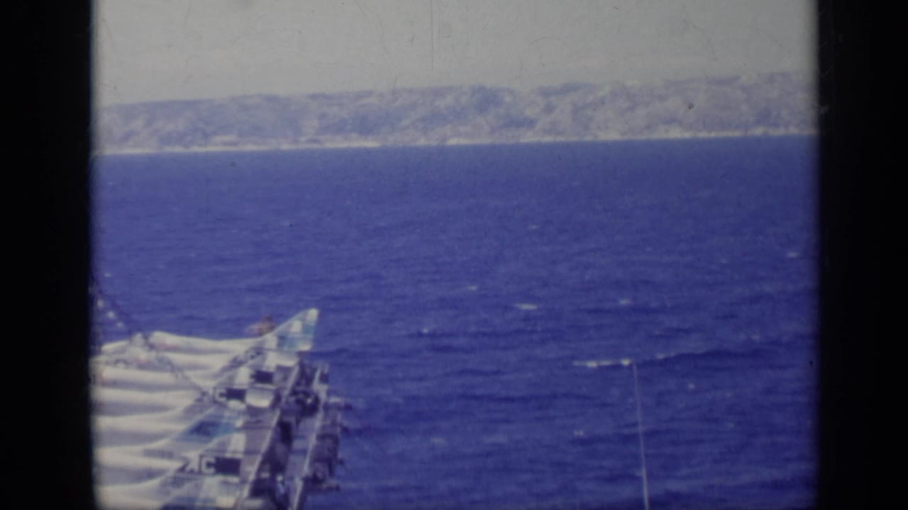 Ship deck equipment at sea with a hazy coastline in the distance.