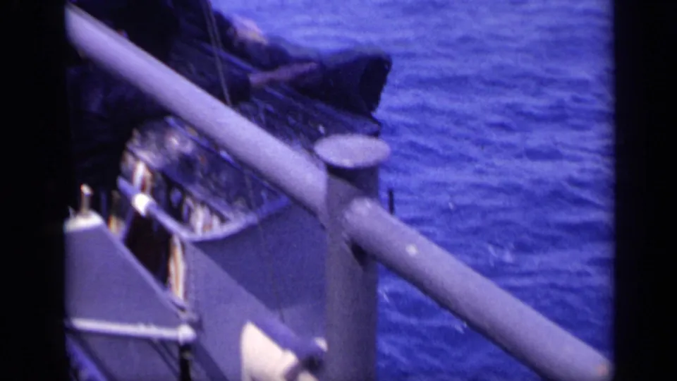 The freighter deck is framed close to a rail and angled deck structure, with rippled blue sea alongside.