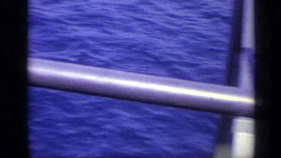 Handheld 8mm view of blue water through gray boat or pier railings in the Italy travel footage.