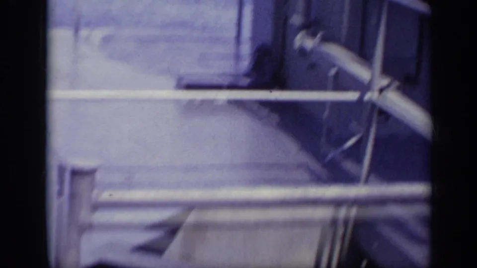 Motion-blurred 8mm frame showing pale boat or dock surfaces with metal bars and dark frame edges.