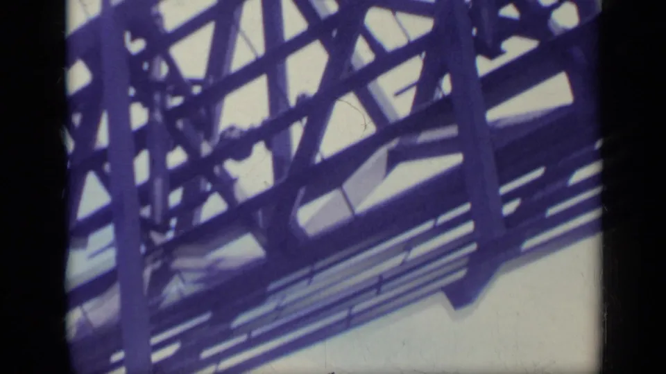 Shipboard 8mm view of dense steel beams and railings, tinted purple-blue, with no people visible.